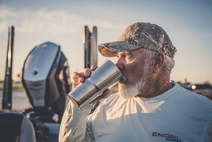 An older man in a cap enjoys a refreshing drink from his Engel Coolers 22oz Stainless Steel Vacuum Insulated Tumbler, part of the Color Collection, while standing outdoors near a vehicle.